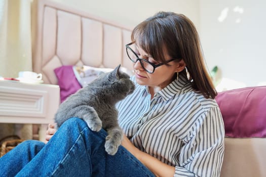 Gray cat in hands of woman at home, cat sitting on knees, woman owner talking touching pet, love friendship, animals people concept