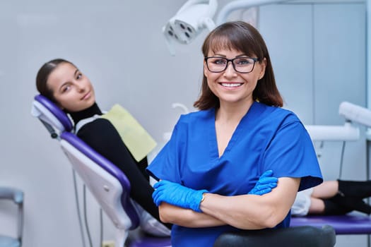Portrait of smiling female dentist looking at camera with young teenage girl patient sitting in dental chair. Visit to dentist examination treatment. Dentistry hygiene dental teeth health care concept