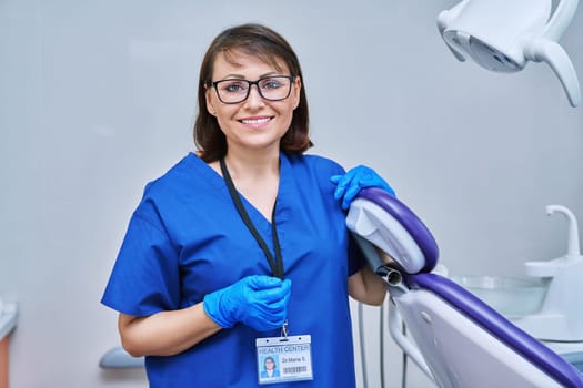 Portrait of smiling female doctor dentist in office. Confident middle aged woman looking at camera near dental chair. Dentistry, examination, occupation, teeth health care concept