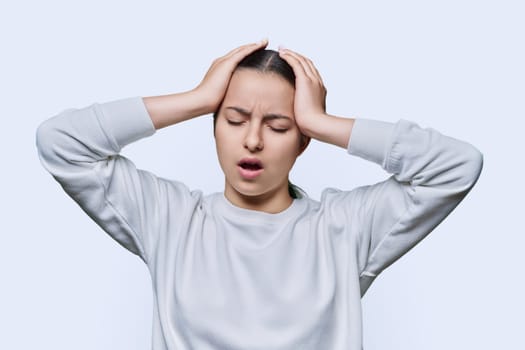 Shocked anxious young woman in panic holding her hands behind her head with her mouth open on white studio background. Teenage student with glasses in hysterics, shock stress helplessness anxiety