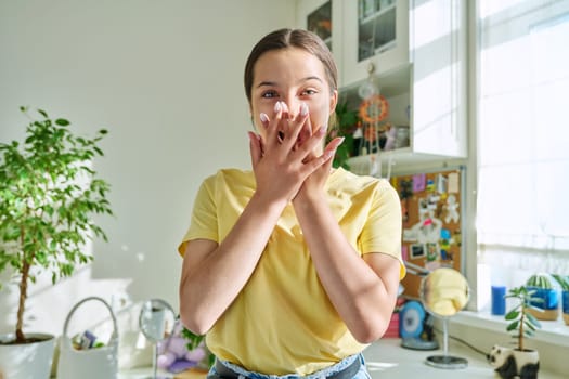 Shocked surprised teenage girl covering mouth with hands looking at camera in home interior. Joy, surprise, shock, wow concept