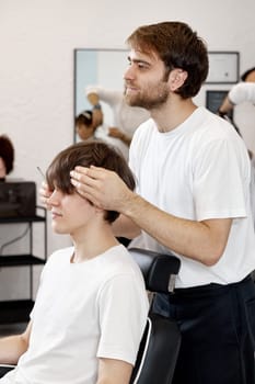 Barber combing caucasian man while sitting in chair before haircut at barbershop. client tells what haircut he wants