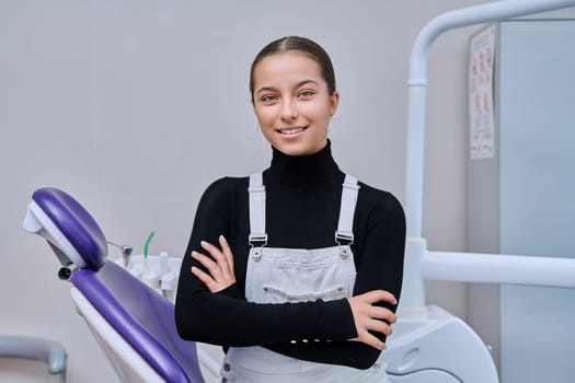 Portrait of young smiling teenage girl in dental chair looking at camera. Teenage female patient in dentist office. Adolescence, hygiene, treatment, dental health care