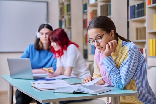 High school students studying in library class, teenage girl in focus. Group of teenagers sitting at desk, writing in notebooks, using laptop books. Knowledge, education, adolescence concept