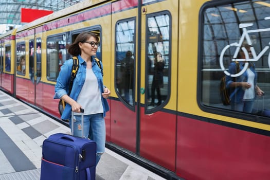 Woman with a suitcase getting ready to board an electric train inside a railway station