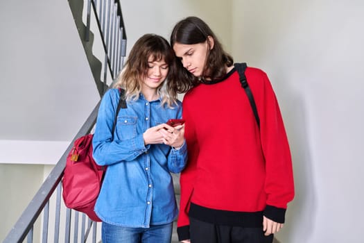 Teenage boy and girl looking at smartphone together. Friends students with backpacks on the stairs inside building. Youth, lifestyle, fashion, style, young people concept