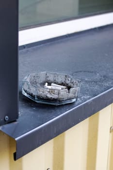 Glass ashtray on the gray windowsill outside close up