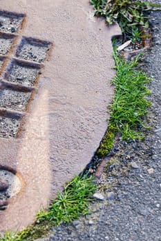 Sewer manhole on the pavement and green grass close up, copy space