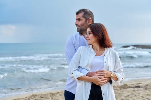 Outdoor portrait of mature couple hugging on beach, background of sea nature, copy space. Middle-aged happy romantic man and woman. Relationships, feelings, lifestyle, marriage, family, people concept
