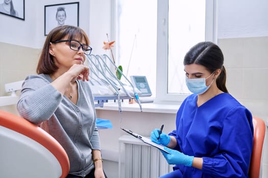 Dental office visit, female patient talking to doctor, dentist making notes for patient treatment. Treatment, dental care, prosthetics, orthodontics, dentistry concept