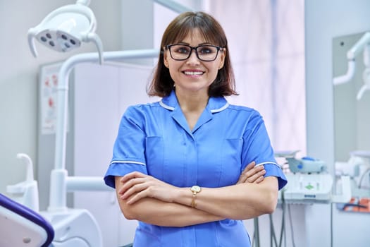 Portrait of smiling nurse looking at camera in dentistry. Confident female with folded hands, dental clinic equipment background. Dentistry, medicine, health care, profession, stomatology concept