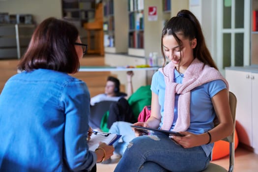 Teenage girl student talking with teacher mentor in the library. Education, knowledge learning, high school, adolescence concept