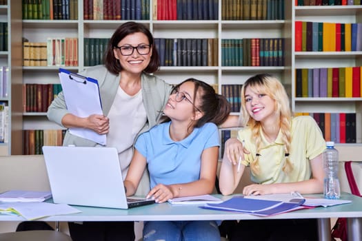 Girls teenage students studying in library with female teacher mentor. High school, education, adolescent, back to school, back to college concept