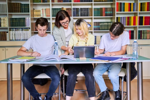 Group of teenage students studying in library class with female teacher. Mentor helping schoolchildren sitting at desks. High school, education, adolescent, back to school, back to college concept