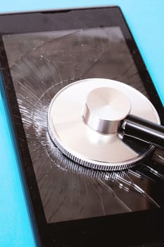 Stethoscope on a broken phone display on blue background close up