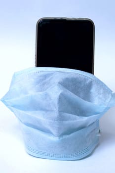 Mobile phone in a medical mask on a gray background, copy space