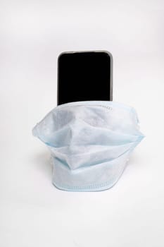 Mobile phone in a medical mask on a gray background