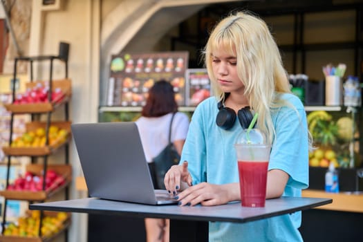 Summer in the city, young teenage woman in outdoor cafe with fruit fresh juice using laptop. Lifestyle, youth, healthy food drinks, leisure concept