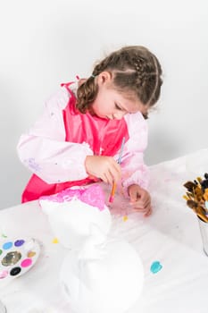 Little girl painting Halloween pumpkin with acrylic paint.