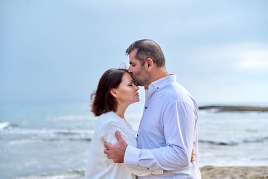 Mature happy loving couple kissing on the sea beach. Wedding, honeymoon, middle aged people relationship, feelings, lifestyle, holidays, dating concept