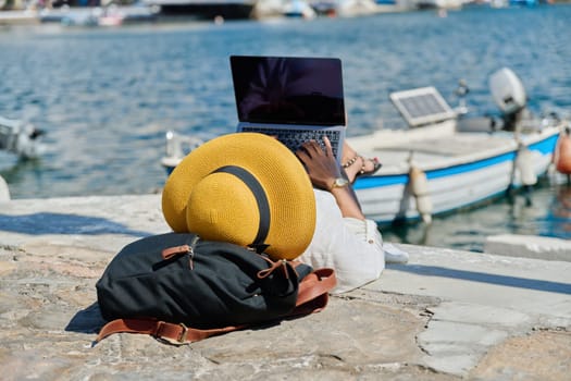 Woman in hat typing on laptop, water bay boat background. Remote work, freelance, tourism, travel, business and entrepreneurship, technology concept