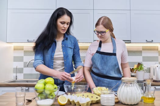 Mother and teenage daughter cooking at home in kitchen. Mom and girl making apple pie together, talking smiling. Relationships, communication parent teenager, healthy homemade food, family concept