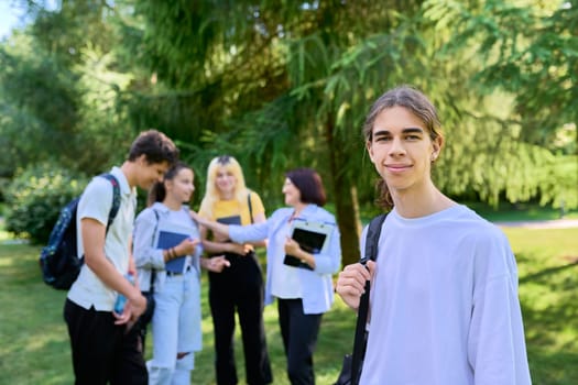 Male student 16, 17 years old with backpack, group of teenagers talking with teacher in school park. Back to school, back to college, high school, education, adolescence, teenage students concept