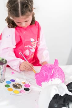 Little girl painting Halloween pumpkin with acrylic paint.