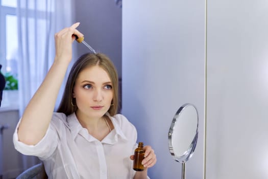Young woman treating her hair using medical drops. Medicine for care and nutrition of hair, from hair loss.
