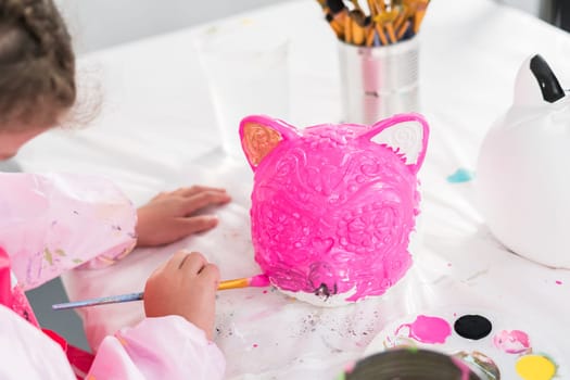 Little girl painting Halloween pumpkin with acrylic paint.