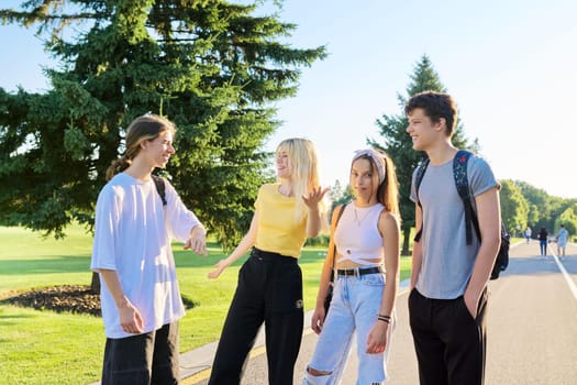 Meeting of smiling teenage friends in sunny summer park. Happy young people greeting each other, hugging, laughing, talking. Friendship, adolescence, communication, emotions, youth concept