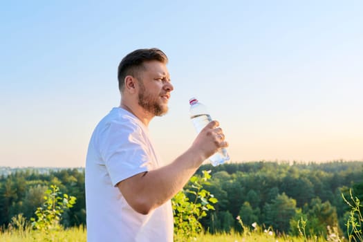 Bearded middle aged man drinking water from a bottle on a hot sunny summer day. Heat, thirst, health, summer concept