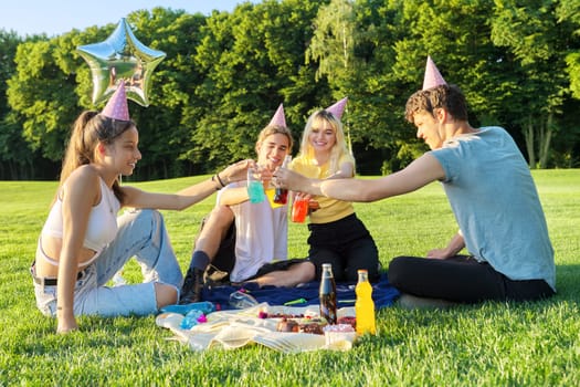 Teenage birthday party picnic on the grass in the park. A group of teenagers having fun, congratulating the girl on her 17th birthday. Age, adolescence, holiday, fun, birthday concept
