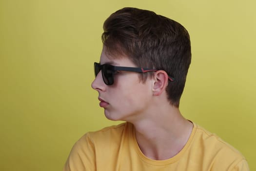 Boy 14-17 years old in a yellow T-shirt in black sunglasses on a yellow background.