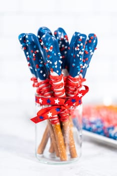 Homemade chocolate-covered pretzel rods decorated like the American flag in a glass jar.