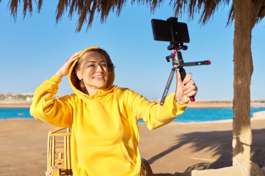 Middle aged woman on the beach talking online using smartphone. Video call, video meeting, chatting, tele technology concept