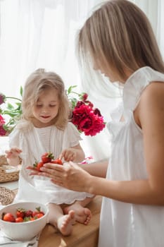 A little blonde girl with her mom on a kitchen countertop decorated with peonies. The concept of the relationship between mother and daughter. Spring atmosphere