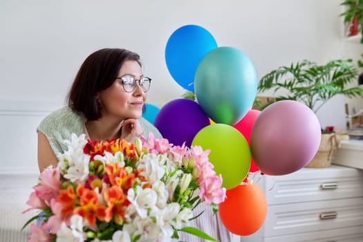 Portrait of a middle aged happy woman with a bouquet of flowers, balloons. Birthday, anniversary, holiday, celebration, people 40s age concept