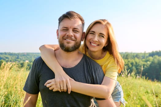 Portrait of happy adult hugging couple on summer sunny day. Beautiful people man and woman embracing in nature, looking at camera, family, happiness, holidays, joy concept