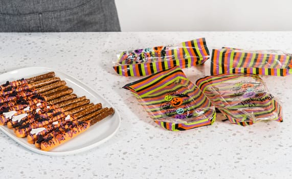 Packaging Halloween chocolate-covered pretzel rods with sprinkles into gift bags.