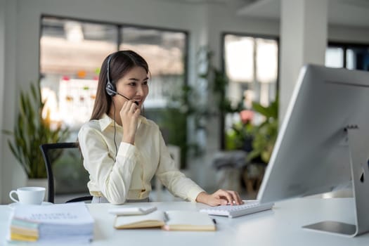 Portrait of happy smiling female customer support phone operator at workplace. Smiling beautiful Asian woman working in call center.