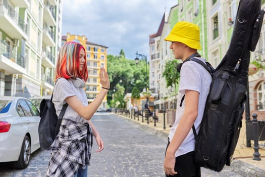 Creative fashionable youth. Talking guy with guitar in case and beautiful girl with trendy dyed colored hair, city street background