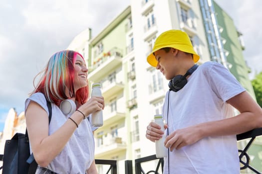 Urban lifestyle of teenagers, couple of college students talking having rest drinking milk drink in bottle outdoors, city street background. Healthy food, youth, recreation and communication concept