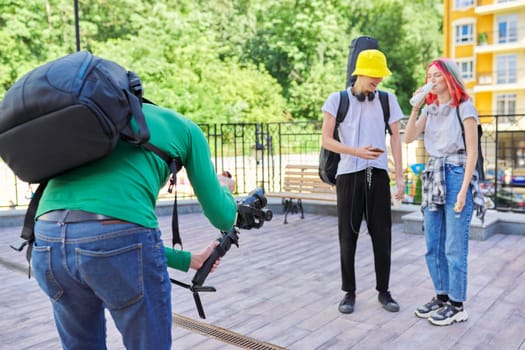 Videographer filming teen models on city. Man using steadicam and camera to make footage. Digital devices for video shoot.