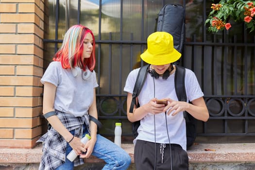 Fashionable modern youth, lifestyle, technology, urban style. Couple of trending teenagers friends with smartphone on city street
