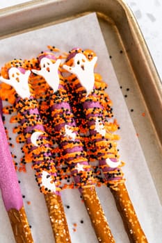 Dipping pretzel rods into melted chocolate to make Halloween chocolate-covered pretzel rods.