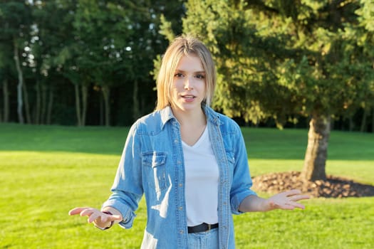 Talking gesturing young woman student looking at the camera. Female webcam recording interview, communicating online using video communication, park nature background