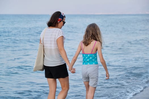 Happy mom and daughter kid walking together on the beach holding hands. Family, vacation, lifestyle, love, weekend concept