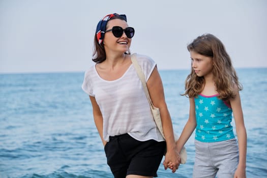 Happy mom and daughter kid walking together on the beach holding hands. Family, vacation, lifestyle, love, weekend concept