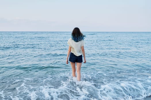 Beauty, nature, youth, freedom concept. Happy beautiful teenager girl enjoying sea water, sea evening nature, back view, looking at the horizon